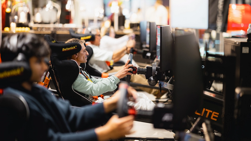 People seated in luxury racing simulator chairs with steering wheels, focused on driving simulations displayed on monitors in front of them, experience the thrill of racing in a premium setting reminiscent of Mallorca’s vibrant atmosphere.