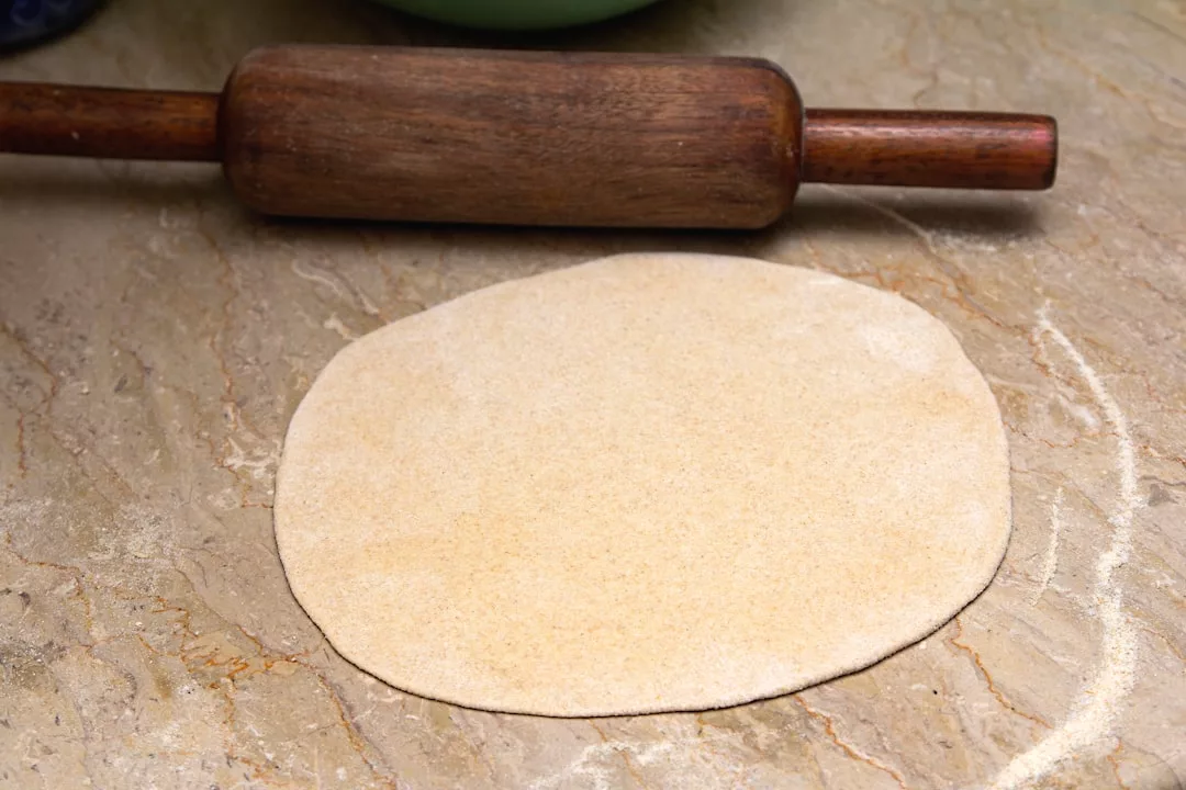A rolled-out dough circle on a floured surface with a wooden rolling pin above it, ready to be transformed into a delicious treat inspired by Mallorcan cuisine found in Valldemossa’s family-owned restaurants.