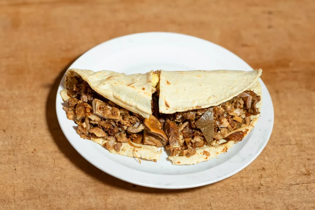 A taco filled with chopped meat and Spanish tortilla, served on a white plate against a wooden background, reminiscent of flavors from Palma's Santa Catalina.