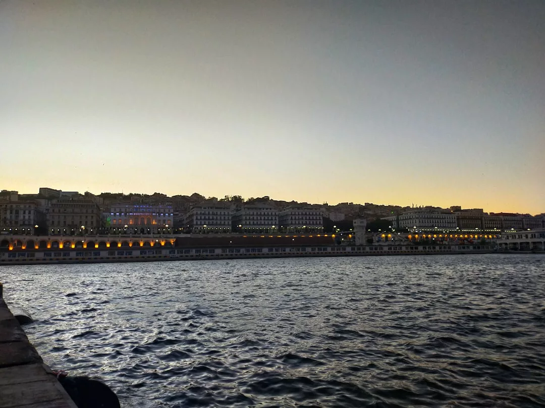 Sunset over Puerto Portals waterfront, with buildings lit by streetlights and gentle waves in the foreground, highlights the marina restaurants and vibrant brunch hotspots along the shore.