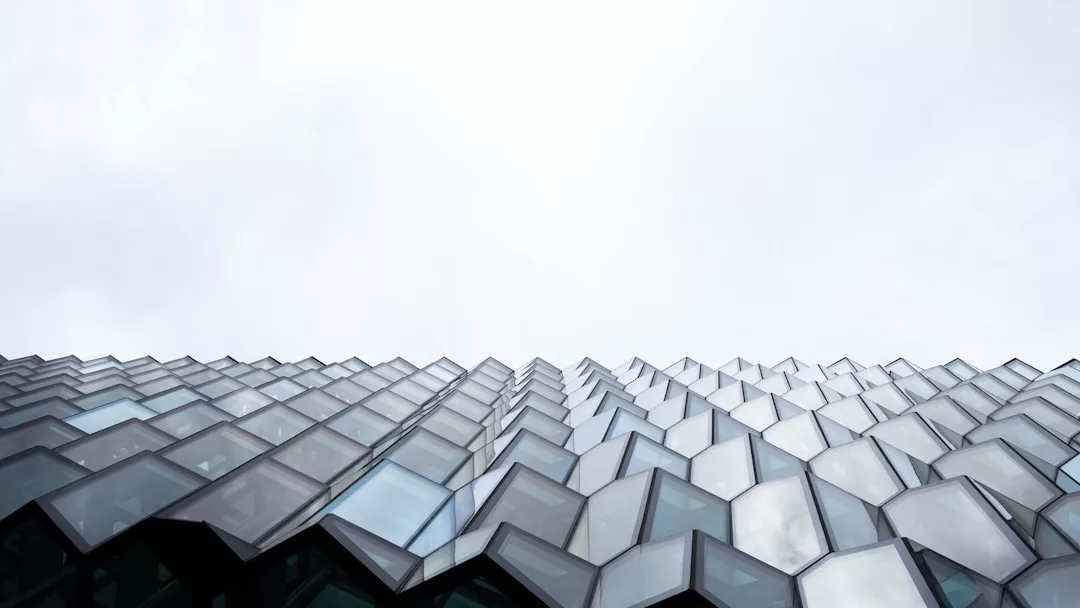 Low-angle view of a contemporary glass house with geometric, honeycomb-like windows, set against a cloudy sky—evoking the modern architecture of Deià with hints of an expansive sea view.