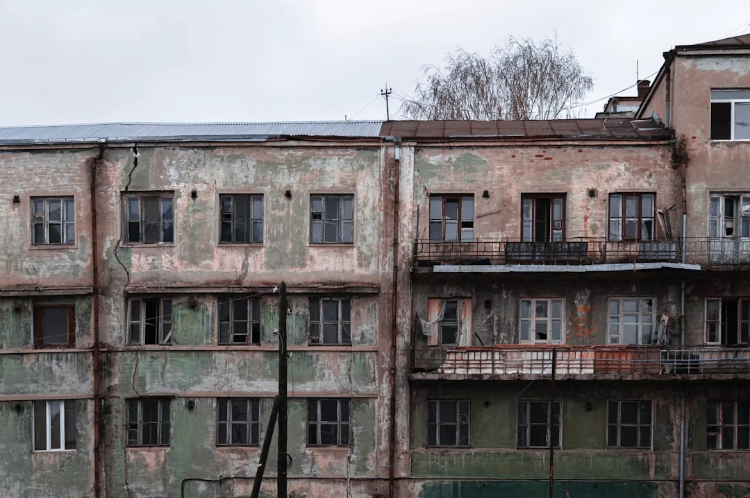 Old, weathered apartment building with peeling paint and broken windows on a cloudy day—far from the eco-luxe villas and green architecture that Estellencs is known for.