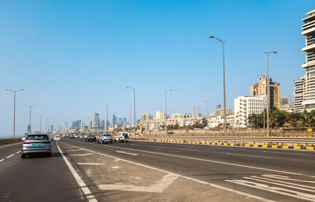 Vehicles drive along a wide city road lined with tall buildings under a clear blue sky, creating an urban scenic drive perfect for memorable itineraries.