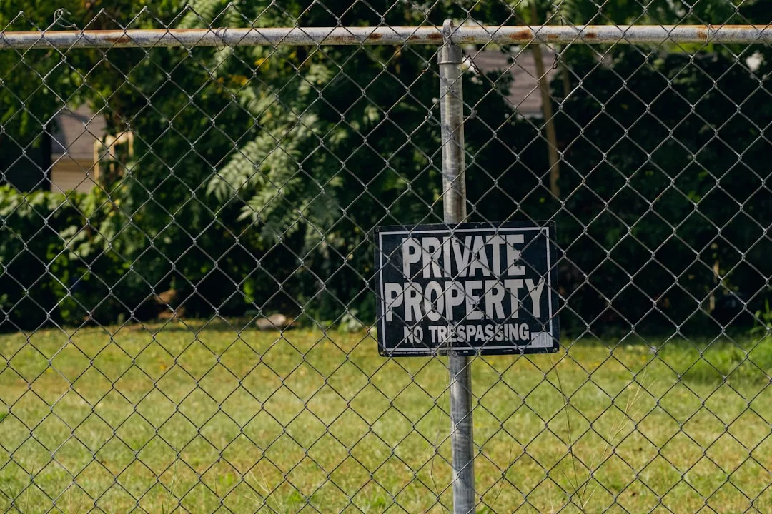 A "Private Property No Trespassing" sign on a chain-link fence highlights property challenges, with grass and trees in the background.