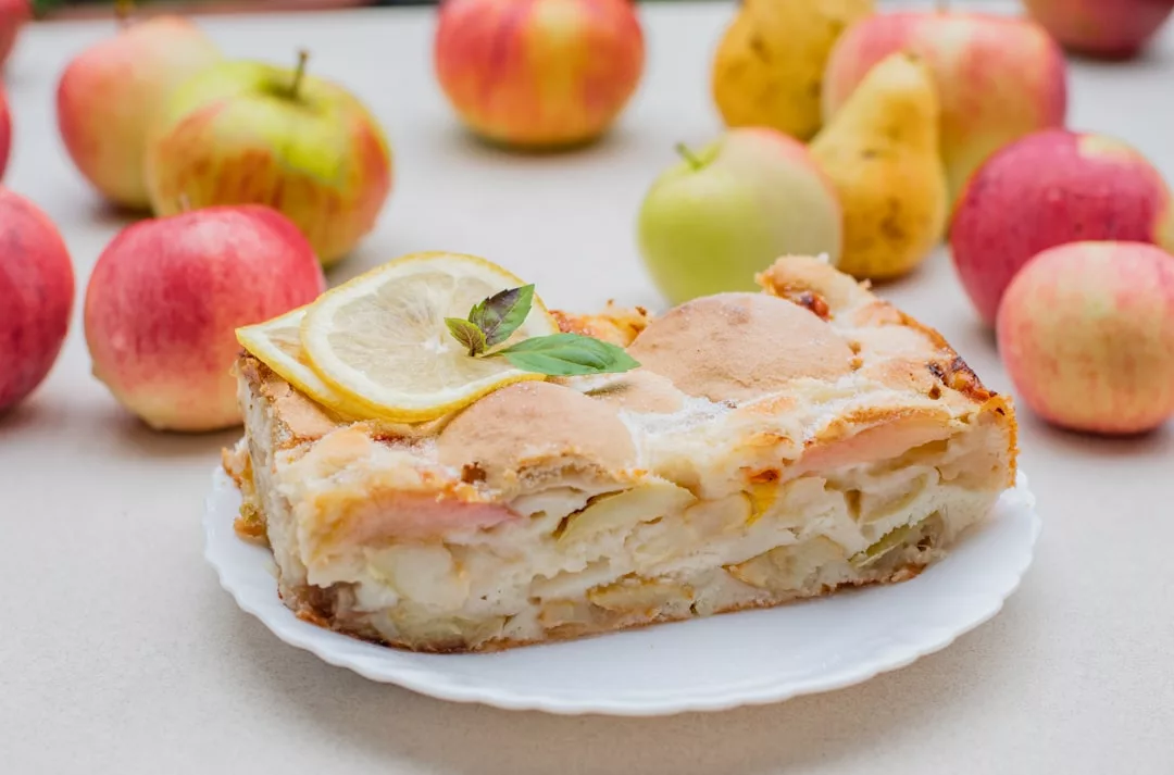 A slice of apple pie with a lemon slice and mint on top, surrounded by apples and pears—a sweet treat inspired by chef-owned fusion restaurants.