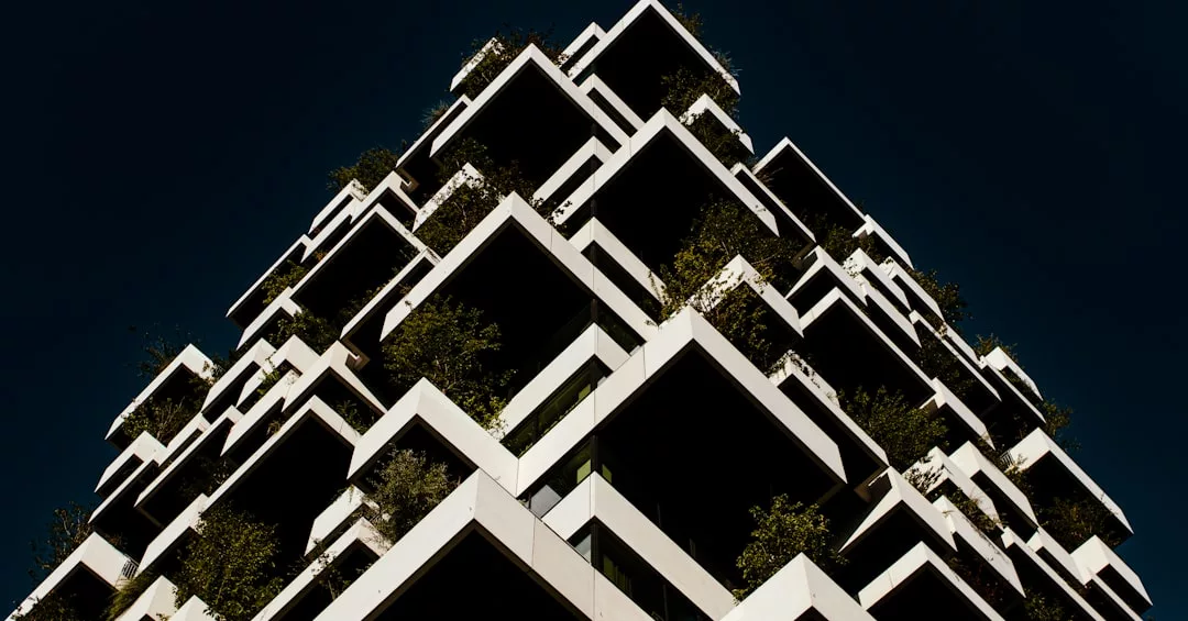 Modern building with staggered, box-like balconies filled with greenery against a dark sky, exemplifying eco-certified construction in Colònia de Sant Jordi.