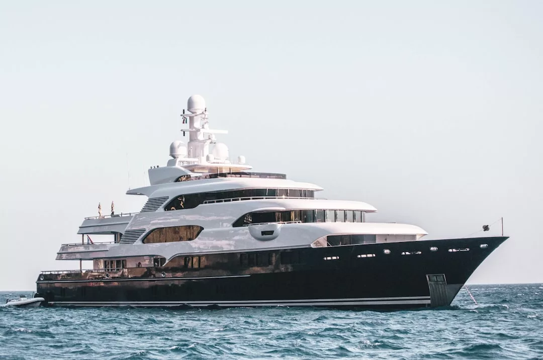 A luxurious white and black yacht floats on the calm blue ocean near Mallorca, basking under a clear sky—perfect for exclusive concert trips.