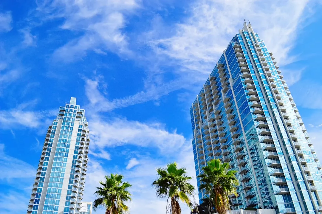 Two tall modern glass buildings with palm trees in front, set against a bright blue sky with wispy clouds—an urban contrast to the serene countryside estates Mallorca is known for.