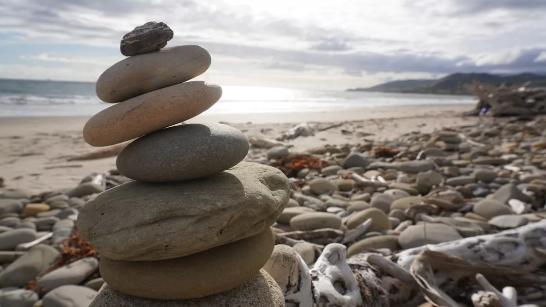 A stack of balanced stones on a rocky beach in south Mallorca, with the ocean and distant hills in the background—a tranquil scene near Colònia de Sant Jordi, perfect for wellness retreats.