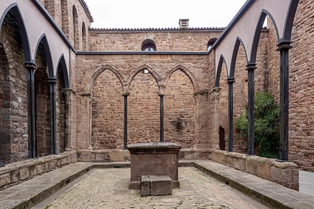 Medieval stone courtyard with arches, columns, and a central well, surrounded by high brick walls—reminiscent of Palma’s iconic Bellver Castle, perfect for a historical tour.