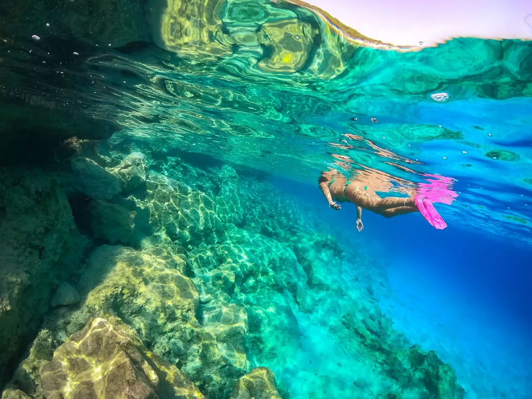 Person snorkeling with pink fins above a vibrant coral reef in clear blue water, sunlight shining overhead—perfect for those seeking private scuba diving or charters in Cala Ratjada.