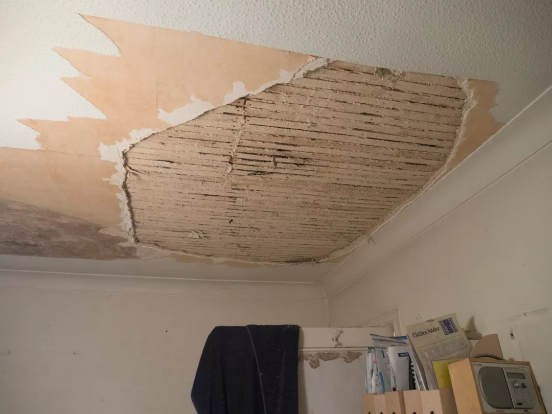 Large patch of peeling ceiling plaster exposes wooden slats in a room with shelves and papers below—an all-too-common sight in Old Town Palma apartments awaiting financing for urgent renovation projects.