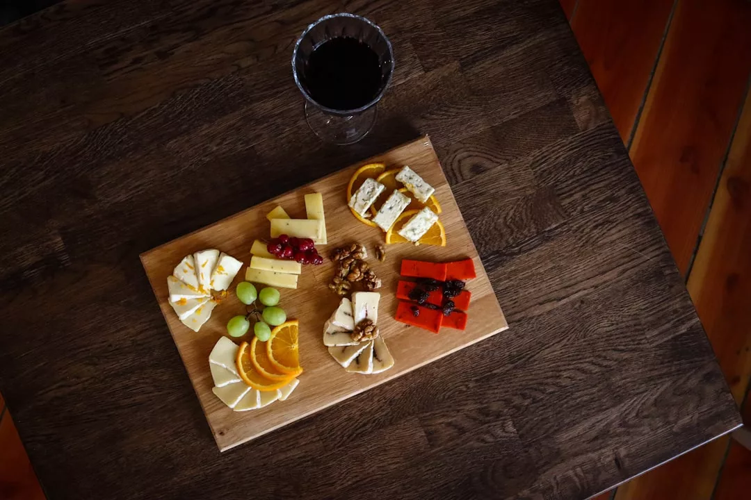 A Nordic-inspired wooden board with assorted cheeses, fruits, nuts, and a glass of red wine on a dark wooden table—perfect for a fine-dining experience.
