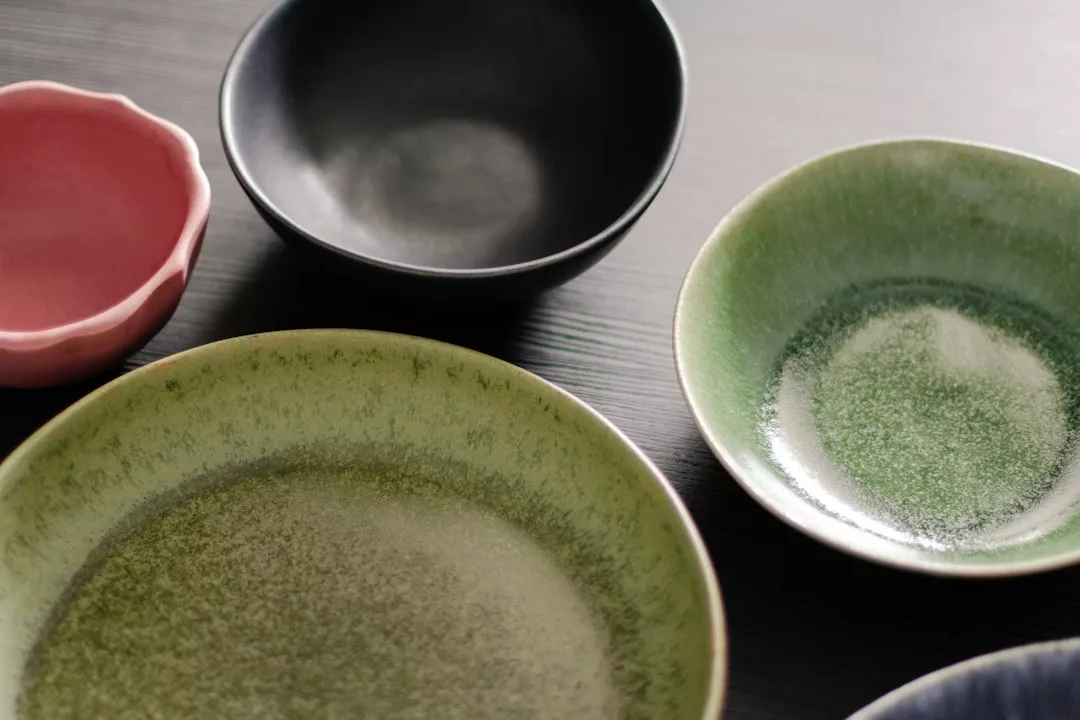 Assorted ceramic bowls in green, black, and pink on a dark surface, viewed from above—perfect for serving fusion-cuisine at stylish pop-ups in Pollença.