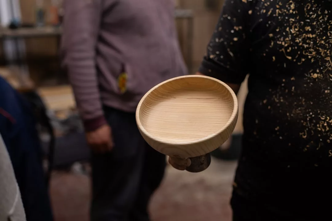 Person holding a handmade wooden bowl, with wood shavings on their clothing in a workshop—crafting unique pieces perfect for gourmet catering events in Santa Ponsa.