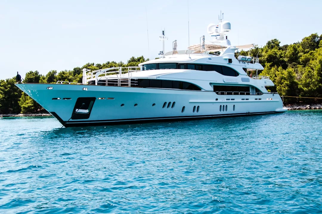 A large white yacht anchored on calm blue water near a forested shoreline under a clear sky, promising glamorous nights reminiscent of exclusive Mallorca party scenes.