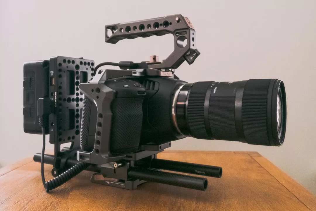 High-end professional video camera rig with handle, lens, and accessories on a wooden surface—perfect for photography safaris or capturing the beauty of Banyalbufar against a plain background.