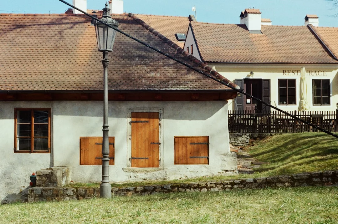 Two rustic buildings with wooden shutters and a lamp post, separated by a grassy yard and stone path—perfect for those exploring Manacor real estate or seeking financing for properties in this charming area.
