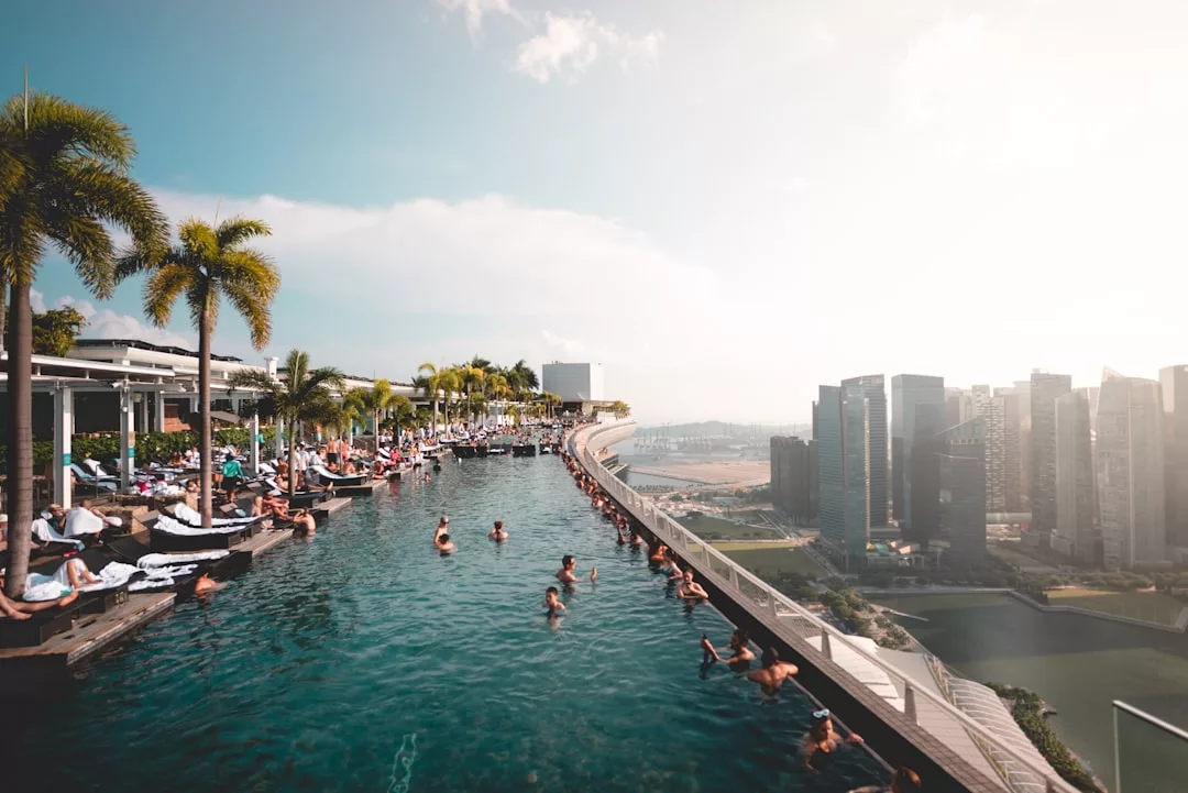 People relax in a luxury rooftop infinity pool overlooking a city skyline, surrounded by palm trees and high-rise buildings.