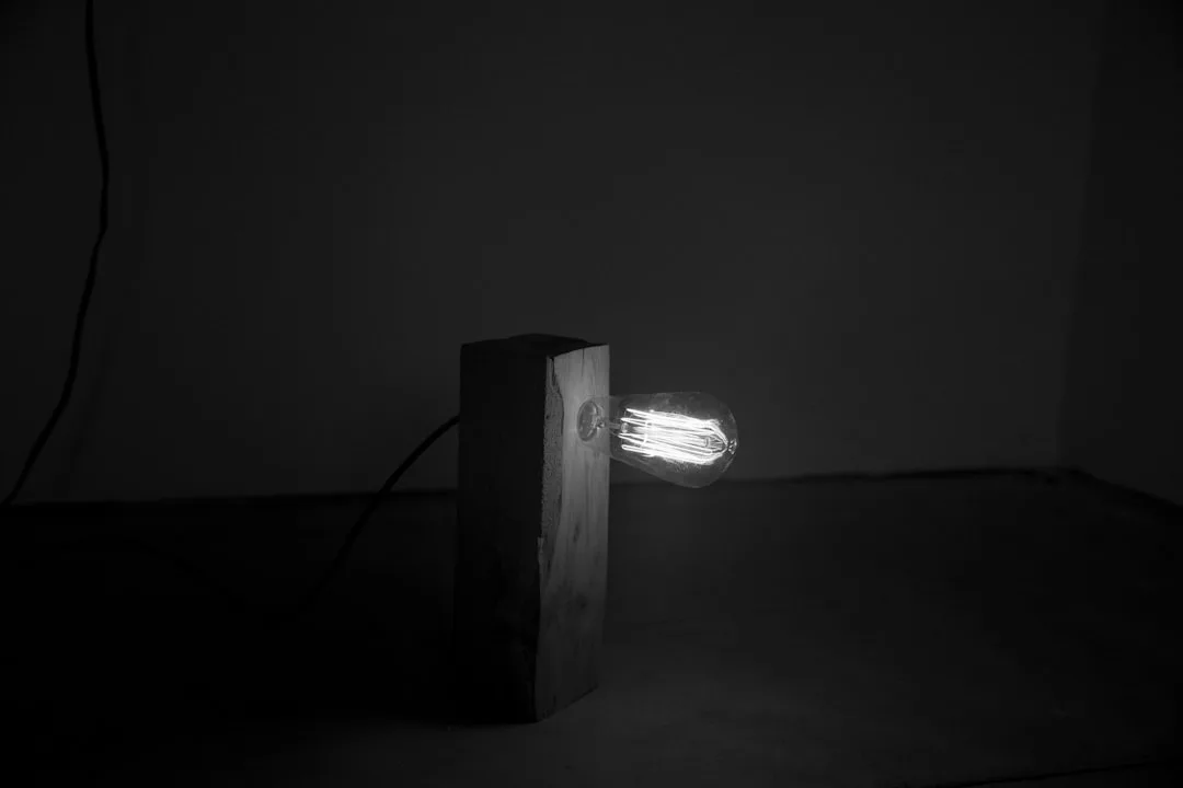 A lit light bulb mounted on a wooden block in a dark, minimalist room—an understated touch perfect for modern homes and refined interior design.