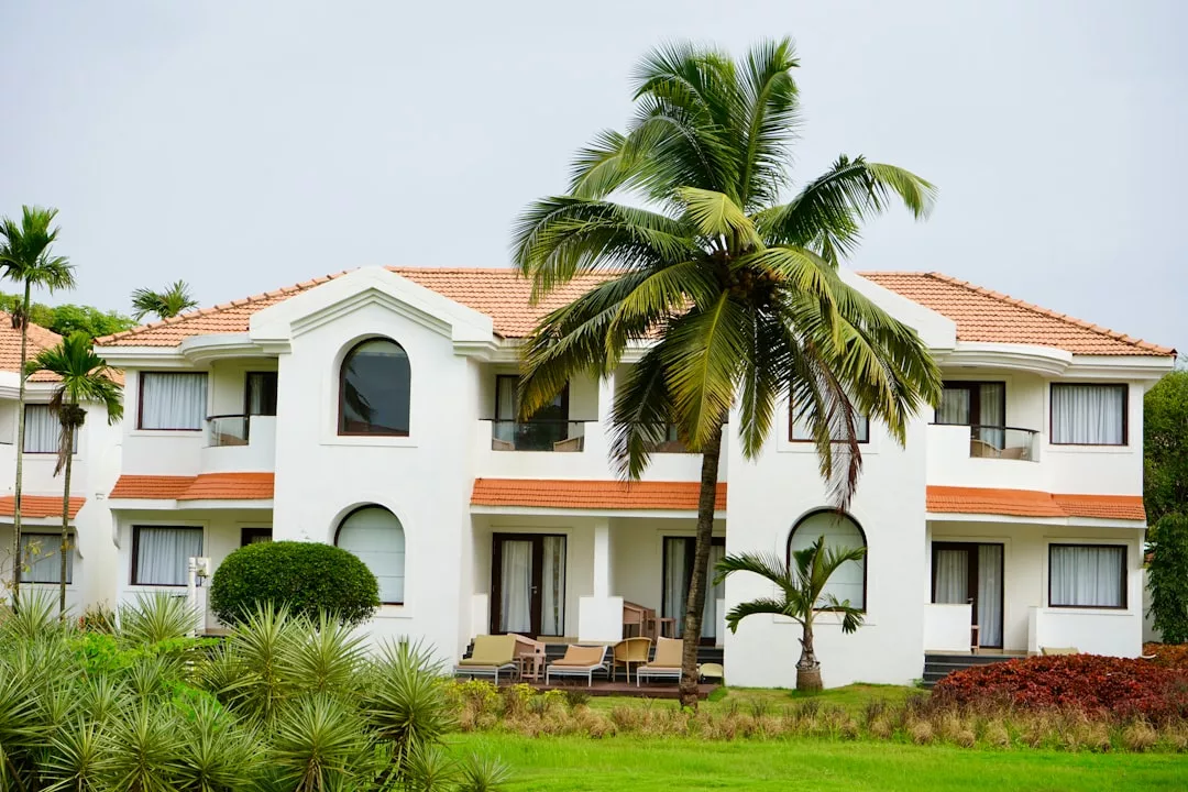 White two-story house with terracotta roof in Camp de Mar, surrounded by palm trees and patio furniture on a green lawn—a perfect spot for investing in holiday resorts.