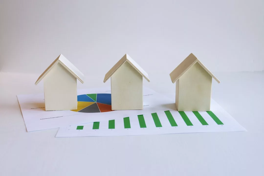 Three small house models on papers with charts and graphs, representing real estate market analysis and legal due diligence for high-value properties.