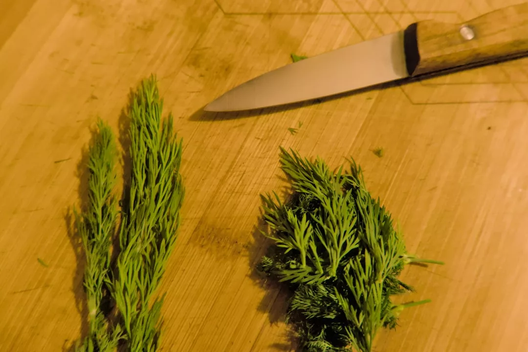 A knife and two small bundles of fresh dill on a wooden cutting board, ready for a luxury meal-kit inspired by Mallorca.