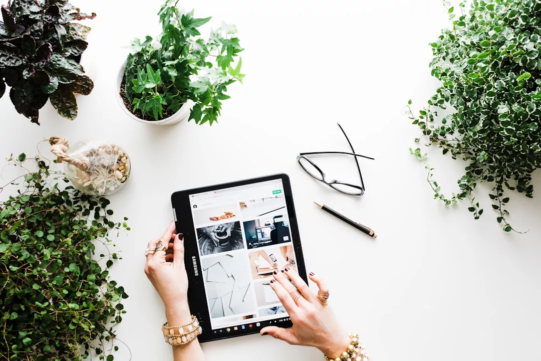 Person browsing a tablet on a white desk surrounded by green plants, glasses, and a pen—researching the latest marketing trends in Cala d’Or and 2025 real estate opportunities.