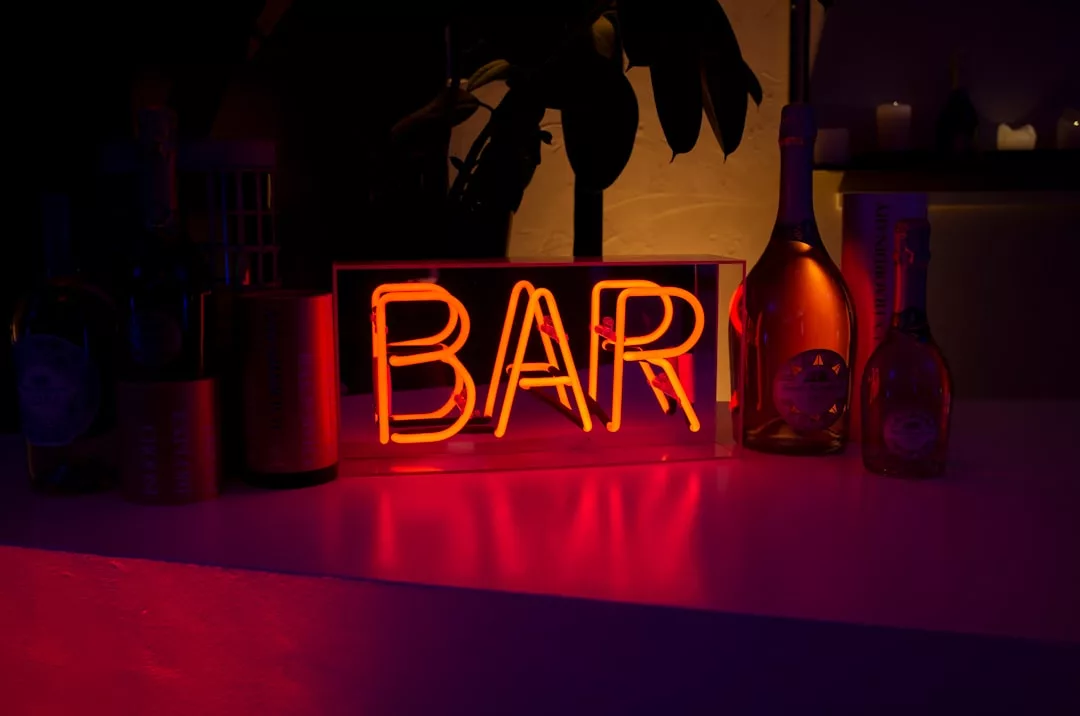 Neon orange "BAR" sign on a counter with bottles and dim lighting in the background, bringing a modern vibe reminiscent of trendy Spanish-cuisine restaurants in Llucmajor.
