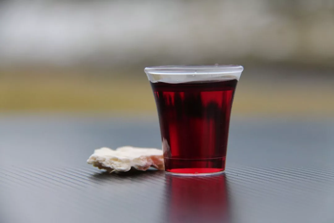 A small plastic cup of red liquid sits next to a piece of bread on a dark surface, reminiscent of quiet moments after negotiating closing costs in Santa María del Camí real estate.