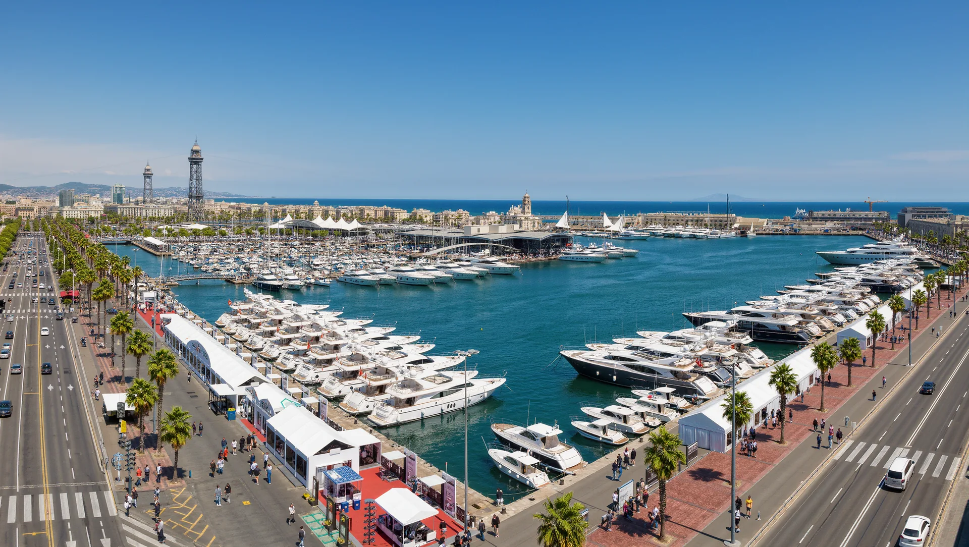 A waterfront boat show on a city quay in spring with yachts along floating pontoons and white exhibition marquees on the promenade.