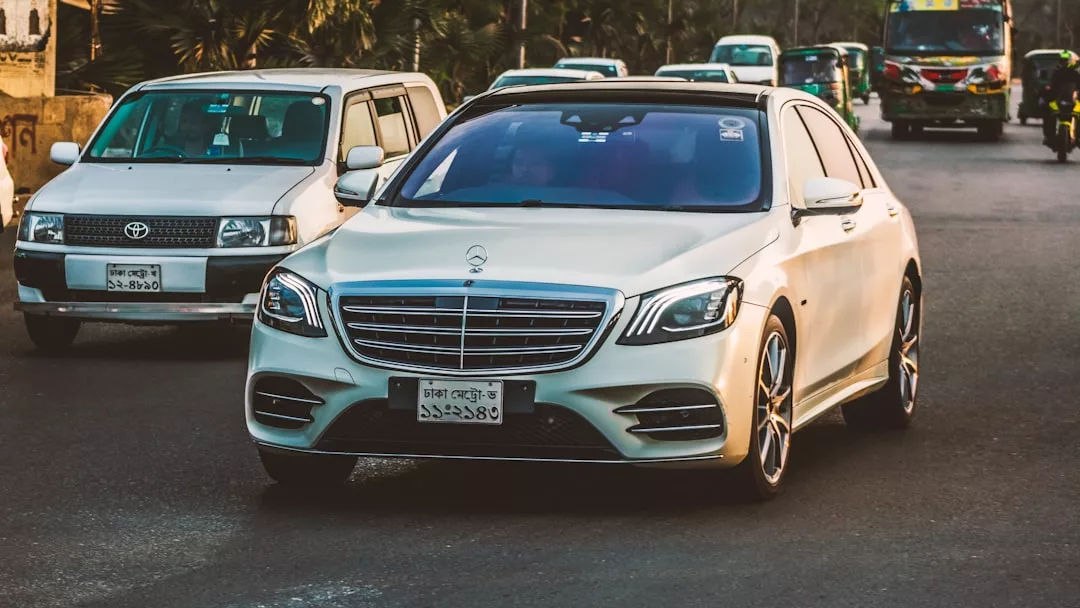 A white Mercedes-Benz sedan, often used for premium chauffeur services in Mallorca, drives on a city street surrounded by other vehicles in daylight.