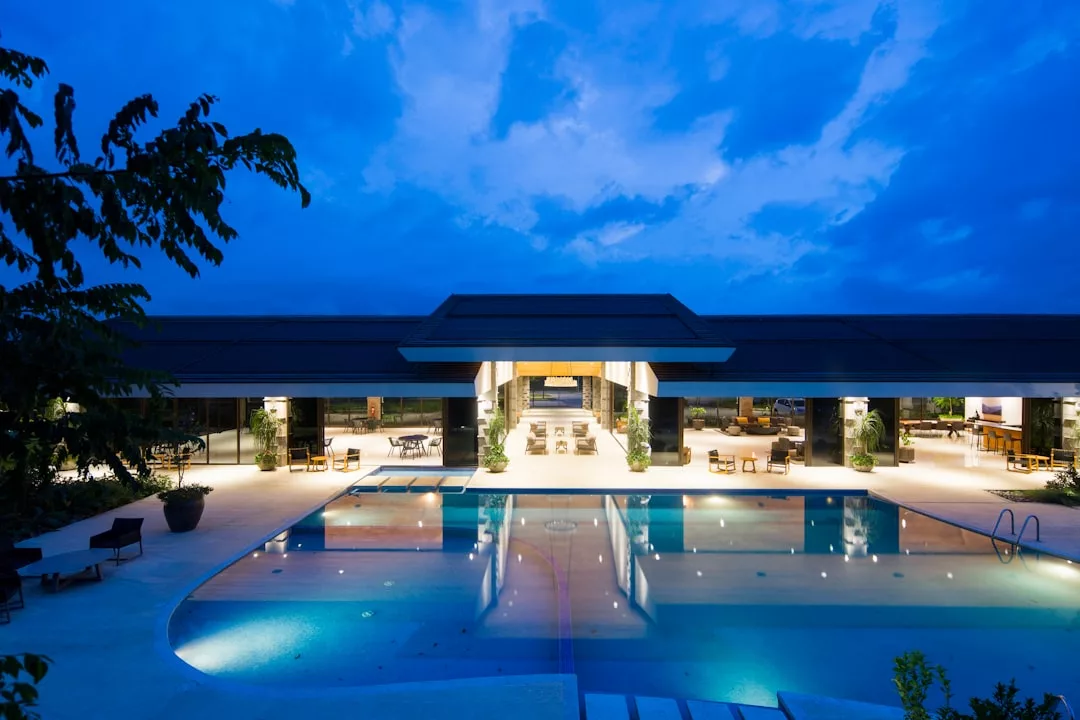 Modern luxury Palma property at dusk, featuring a large illuminated swimming pool and open patio under a dramatic blue sky—perfect for those seeking expert real estate advisory on premium property purchases.