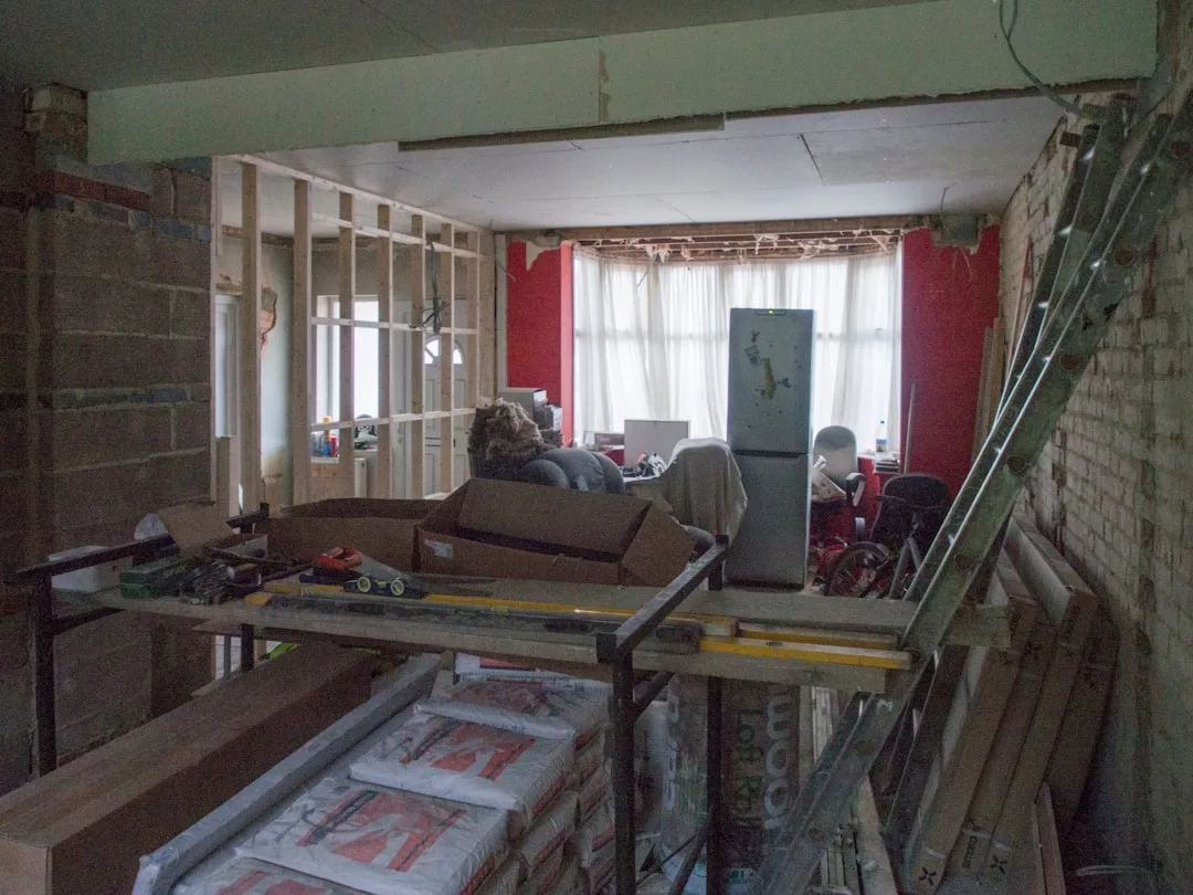 A cluttered room in Ses Salines is under renovation, with exposed walls, tools, ladders, and furniture near a large window—a perfect scene to use a renovation cost estimator for fincas.