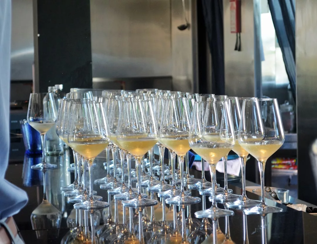 Rows of wine glasses filled with white wine lined up on a reflective black counter in a modern bar, reminiscent of the chic rooftop wine bars found in Palma's vibrant La Rambla district.