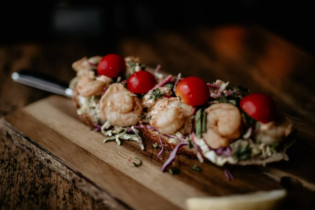 Open-faced seafood sandwich with shrimp, cherry tomatoes, and greens on a wooden board, with a lemon wedge nearby—a perfect bite to enjoy while exploring Porto Petro restaurants or considering cava pairings.