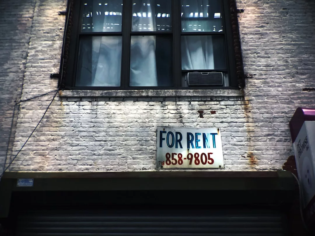 A "For Rent" sign with a phone number hangs on a white brick building below a window, attracting the attention of real estate agents Palma and foreign buyers alike.