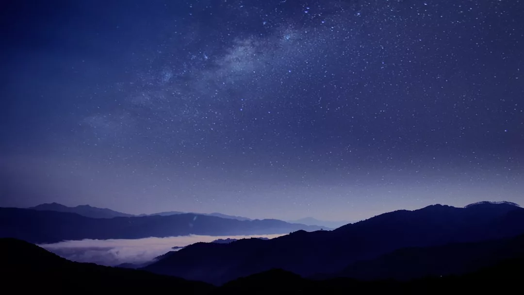 Starry night sky over dark mountain silhouettes with mist covering the valleys, perfect for stargazing near Es Pontàs in Santanyí.