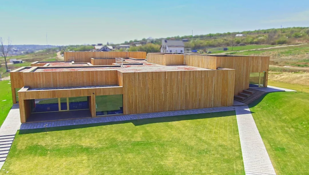 Modern, flat-roofed wooden building with large windows, surrounded by grass and walkways—an example of sustainable estate developments in Port d’Alcúdia.