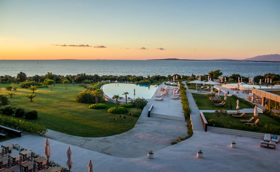 Resort pool and lounge chairs overlook the ocean at sunset, surrounded by green lawns and palm trees in Mallorca’s exclusive Portals Nous, offering a serene escape with access to a luxury spa.