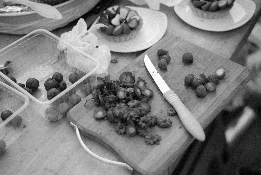 Black and white image of strawberries being sliced on a cutting board with a knife, berry tarts nearby—perfect for capturing the essence of Sóller’s tasting experiences.