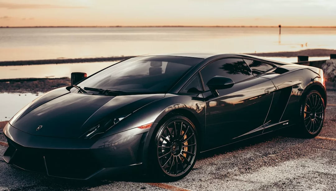 A black Lamborghini parked by the water at sunset in Mallorca, its sleek surface reflecting the golden sky—perfect for those dreaming of luxury road trips along the stunning Serra de Tramuntana.