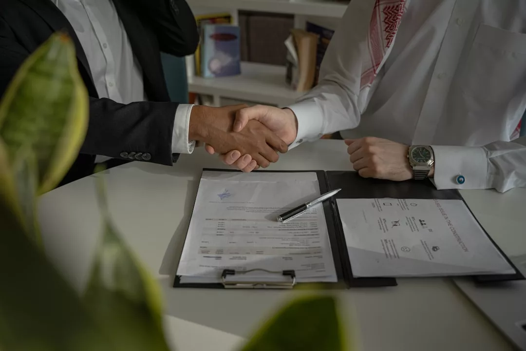 Two people in business attire shaking hands over a contract on a desk, with a pen and documents visible—finalizing details about Cala Sant Vicenç property and landlord regulations.