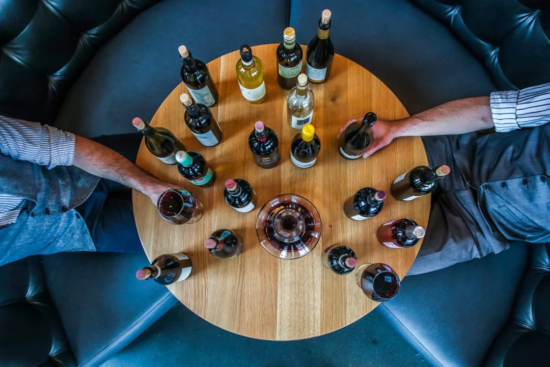 Two people sit at a round table in Santa María del Camí, surrounded by wine bottles and glasses, enjoying a leisurely lunch reminiscent of vineyard tours.
