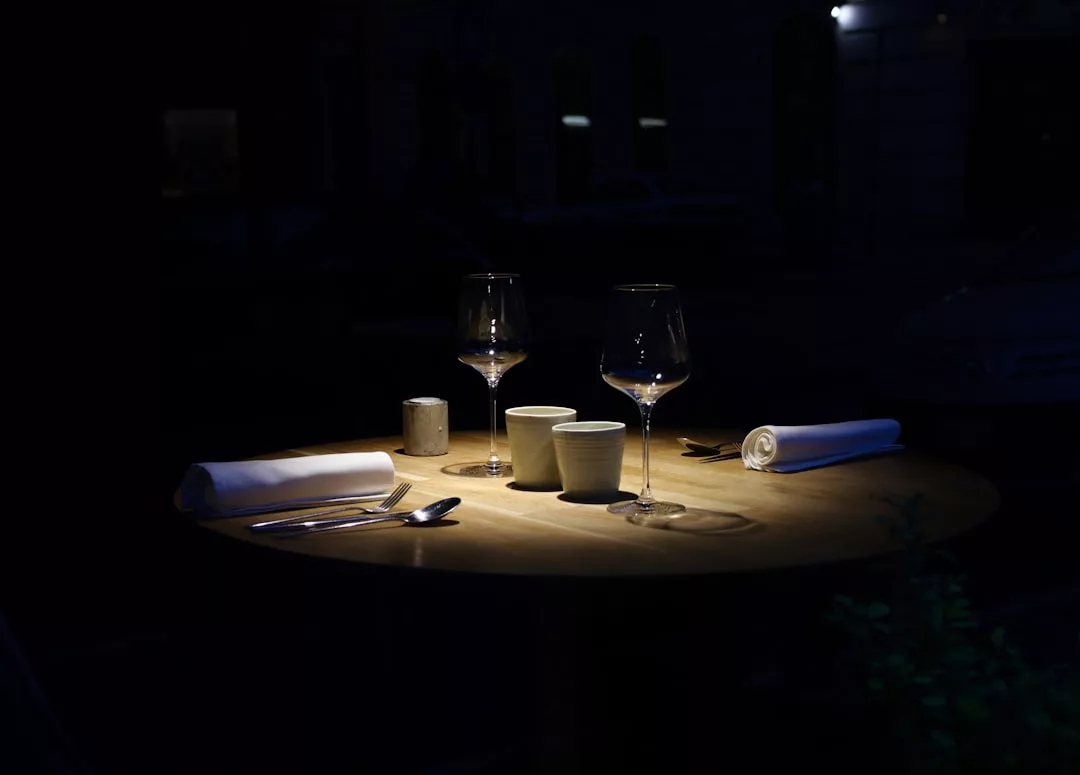 A dimly lit table set for two with glasses, napkins, and utensils in a dark wine-bar restaurant reminiscent of the vineyards near Santa María del Camí.