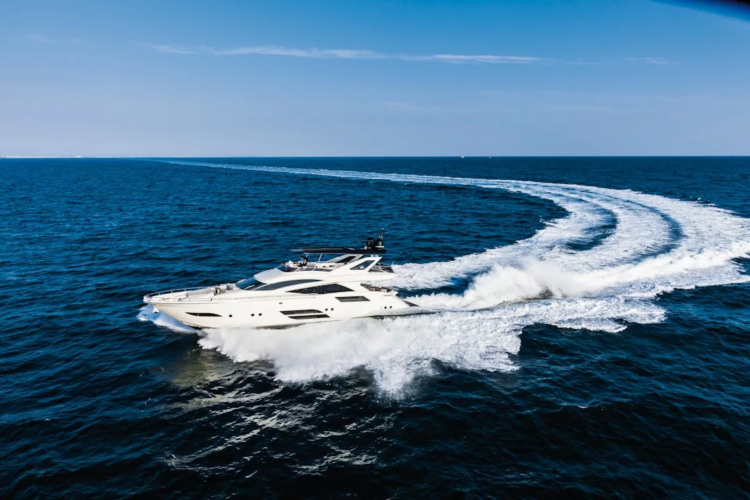 A white yacht speeds across the blue ocean within Cabrera marine park, leaving a curved trail of white waves behind it under a clear sky.