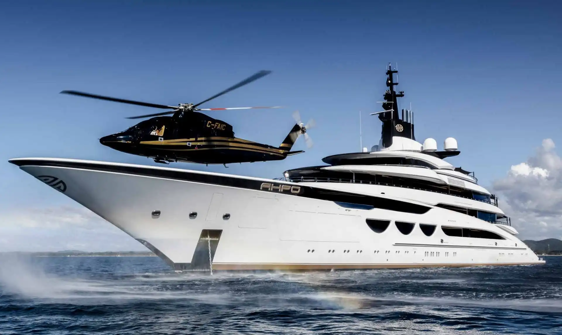 A black helicopter is landing on the bow of the luxury yacht AHPO, which is floating on calm blue water near Mallorca.