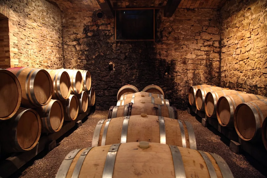 A stone-walled wine cellar with wooden barrels arranged in rows along the walls and center, lit by warm overhead lighting, exuding a sense of luxury and refined lifestyle.