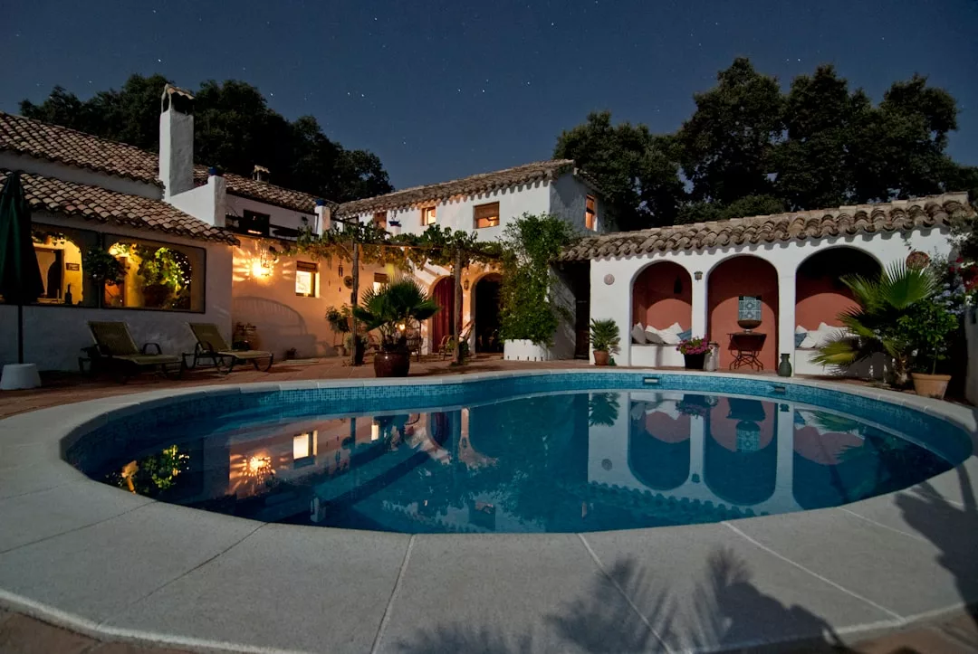 A circular swimming pool in the courtyard of a Mediterranean-style house in Majorca at night, with outdoor lights and surrounding greenery, creates a scene of relaxed luxury and sophisticated lifestyle.