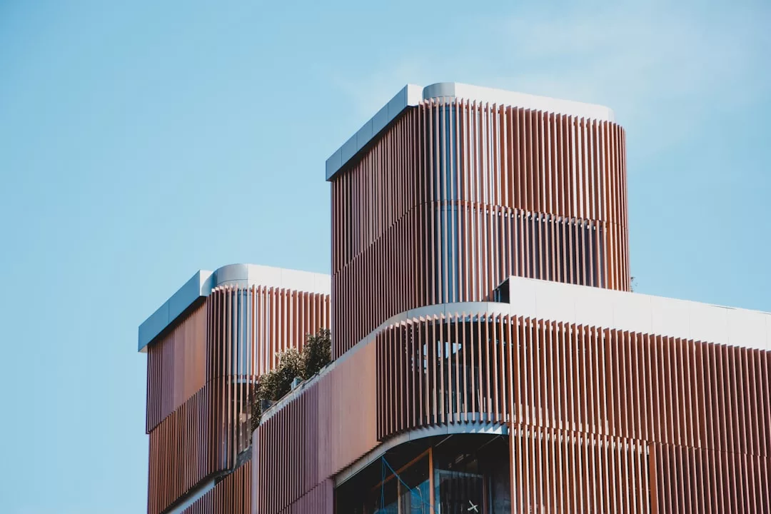 Modern luxury building with multiple levels featuring vertical wooden slats and rounded edges, embodying an elevated lifestyle against a clear blue Majorca sky.